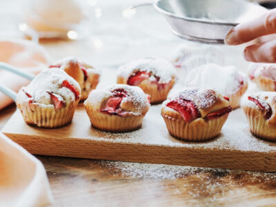 Person sprinkles powdered sugar on freshly baked strawberry cupcakes at the home kitchen. Soft focus.